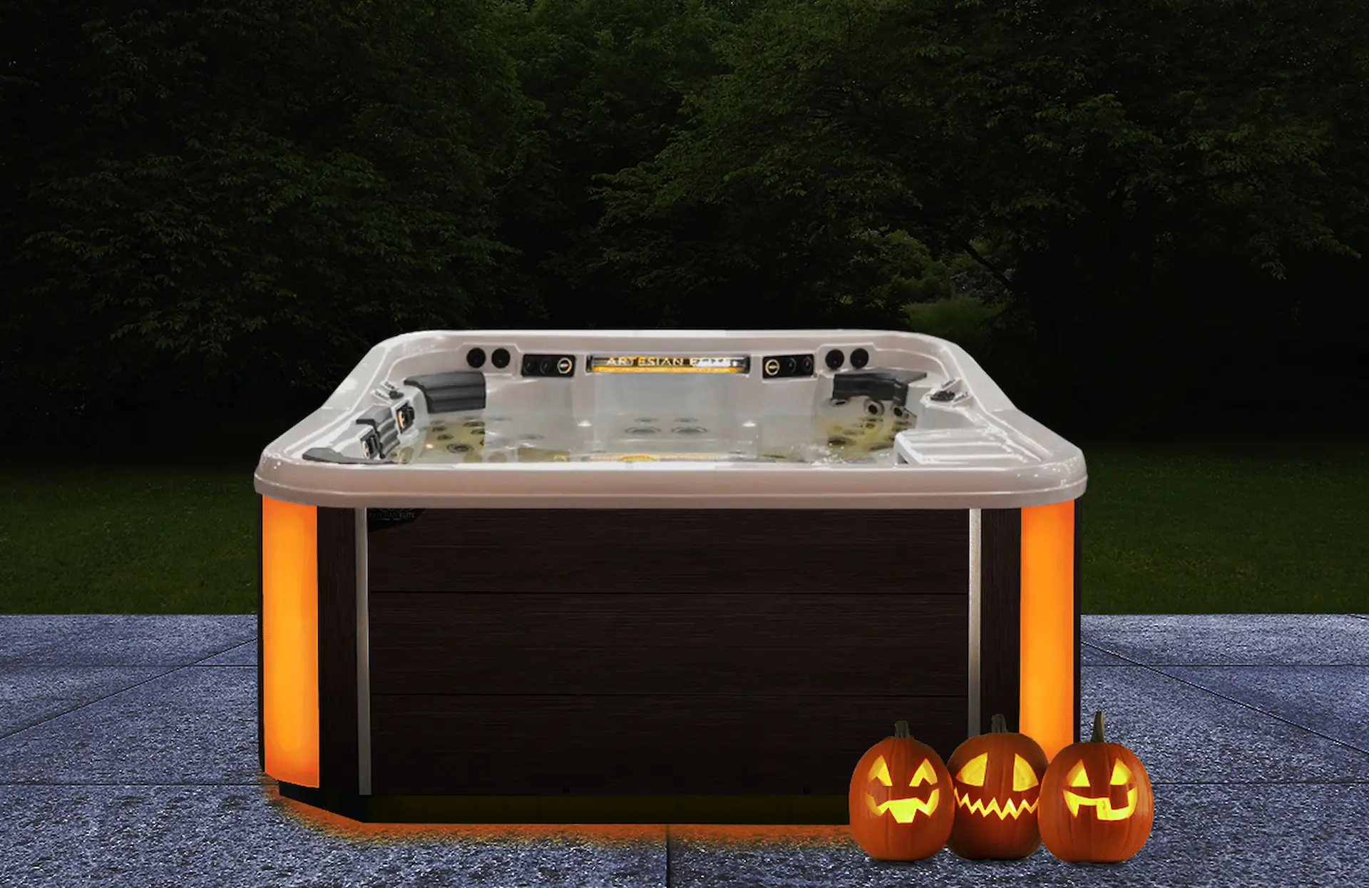 Medium shot of a hot tub with orange light panels running vertically on the corners of the tub's frame. Three jack-o-lanterns sit by the bottom of the hot tub in the lower right-hand corner. A Halloween party in a hot tub like this requires Halloween Games to Play in Your Hot Tub.
