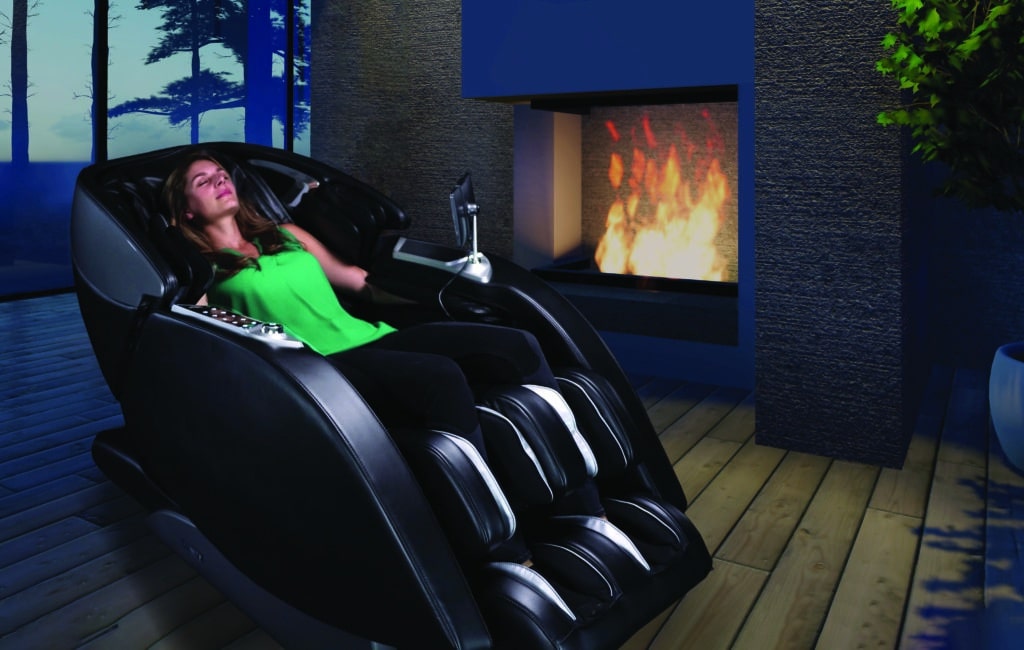 woman relaxes in a black massage chair in her home in front of a warm fireplace